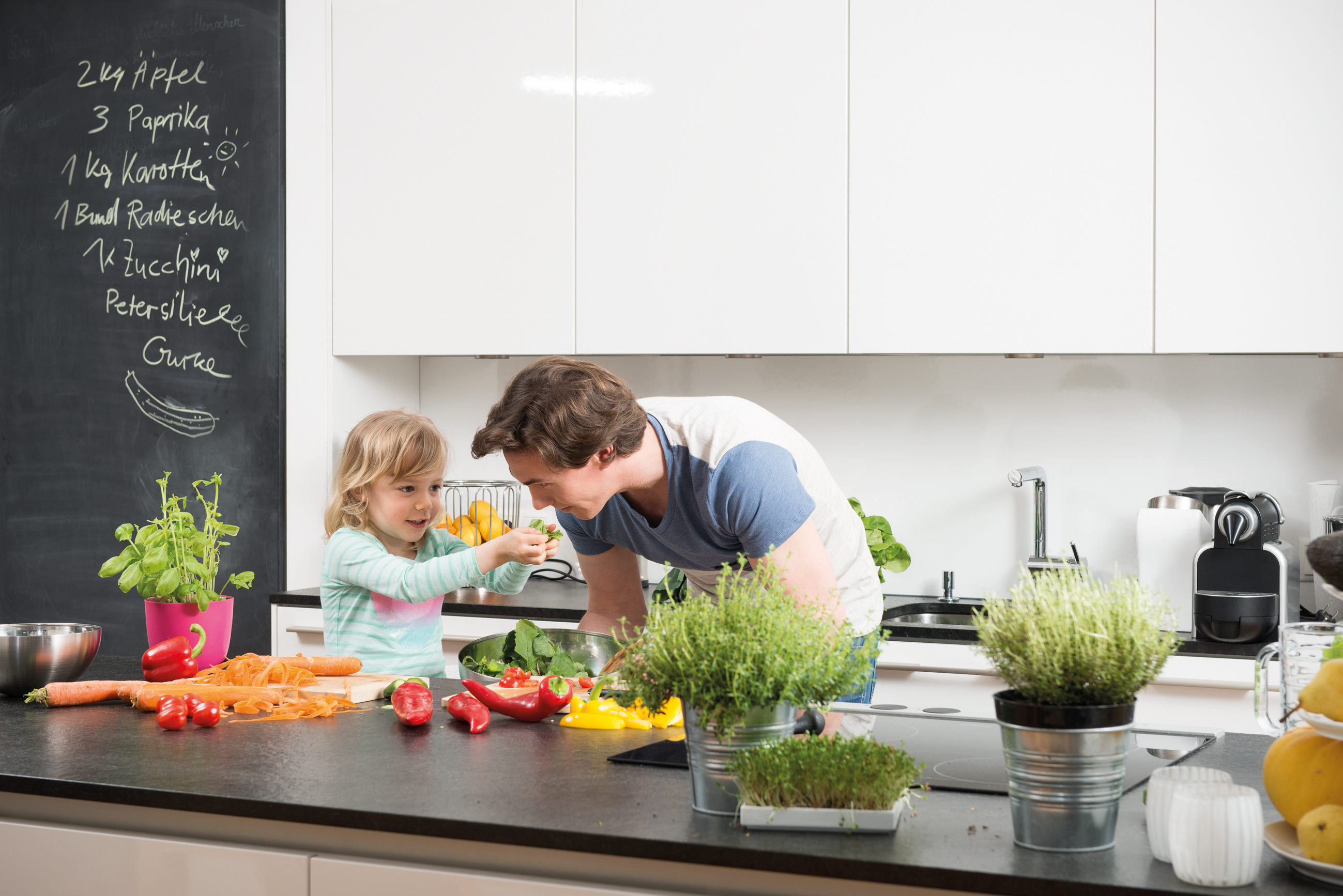 Otac i dijete u kuhinji za radnom površinom pripremaju hranu, na ploči povrće i začini